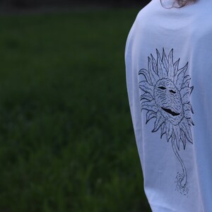 May include: White long-sleeve t-shirt with a black and white graphic of a stylized sun with a face on it.