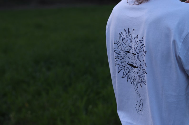 May include: White long-sleeve t-shirt with a black and white graphic of a stylized sun with a face on it.