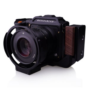 May include: A black Hasselblad camera with a large lens and a wooden grip. The camera has a silver inscription that reads "HASSELBLAD".