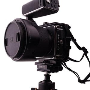 Könnte beinhalten: Eine schwarze Hasselblad-Kamera mit einem Objektiv und einem schwarzen Blitz oben. Die Kamera ist auf einem Stativ montiert.