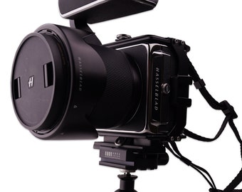 Könnte beinhalten: Eine schwarze Hasselblad-Kamera mit einem Objektiv und einem schwarzen Blitz oben. Die Kamera ist auf einem Stativ montiert.