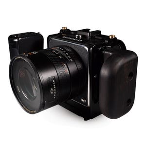 Könnte beinhalten: Eine schwarze Hasselblad-Kamera mit einem schwarzen Objektiv und einem Holzgriff. Die Kamera hat eine silberne Verzierung und das Objektiv hat eine Tiefenschärfenskala.