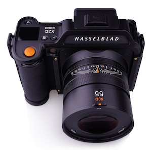 K&ouml;nnte beinhalten: Eine schwarze Hasselblad X2D Kamera mit einem schwarzen XCD 55mm Objektiv. Die Kamera verf&uuml;gt &uuml;ber ein digitales Display und verschiedene Kn&ouml;pfe und Drehregler. Das Objektiv hat eine Tiefensch&auml;rfenskala und einen Blendenring.