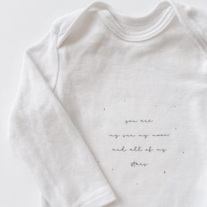 Könnte beinhalten: Weißer Langarm-Baby-Strampler mit dem Aufdruck "You are my sun my moon and all of my stars" auf der Vorderseite.