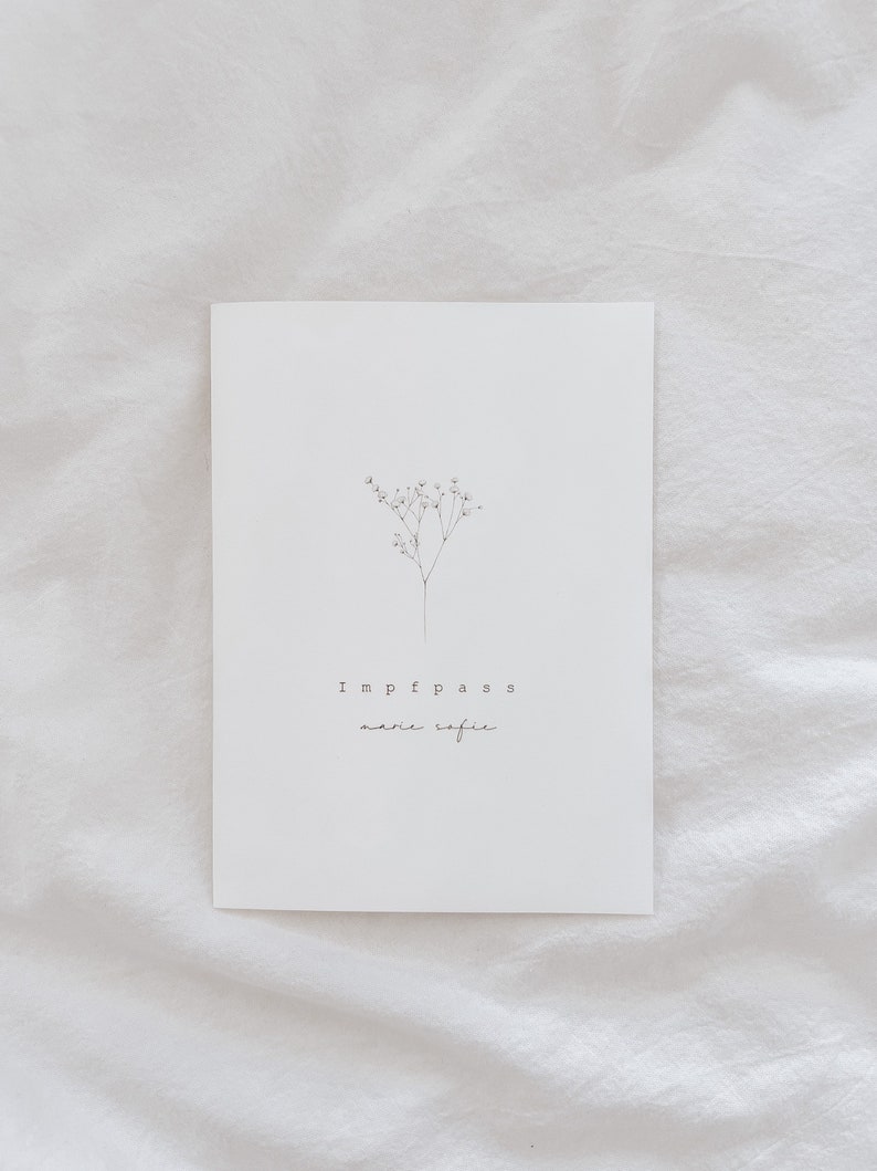 May include: A white card with the words "Impfpass marie sofie" in a minimalist font. A delicate, black line drawing of a small flowering plant is above the text. The card is set against a white, textured background.