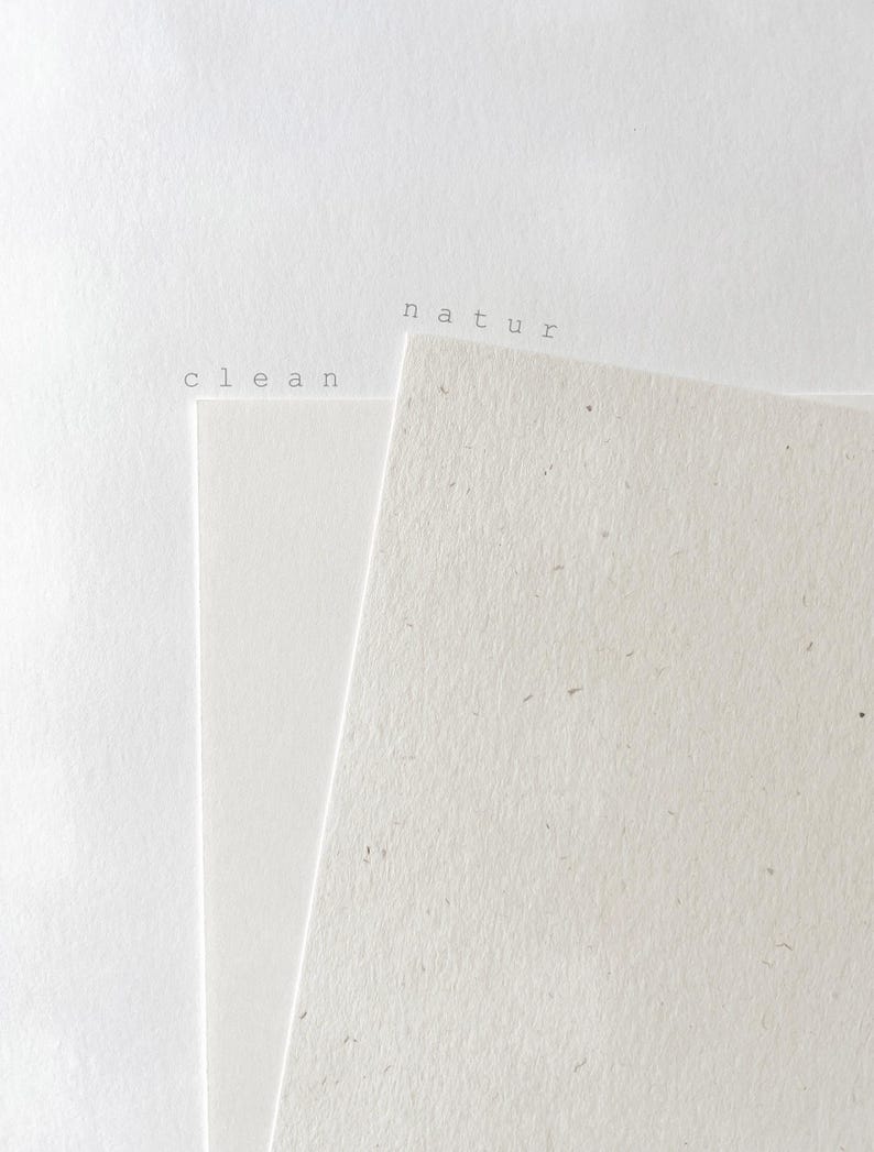 May include: Two sheets of paper are layered. The left sheet is smooth, bright white, and labeled with the word clean. The right sheet is off-white, textured with visible flecks, and labeled with the word natur. Both labels are in black.