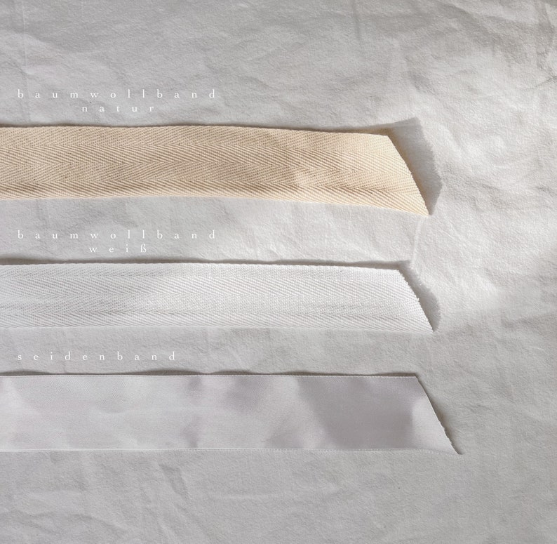 May include: Three different types of ribbon: natural cotton ribbon, white cotton ribbon, and white satin ribbon. The ribbons are labeled "baumwollband natur", "baumwollband wei&szlig;", and "seidenband".