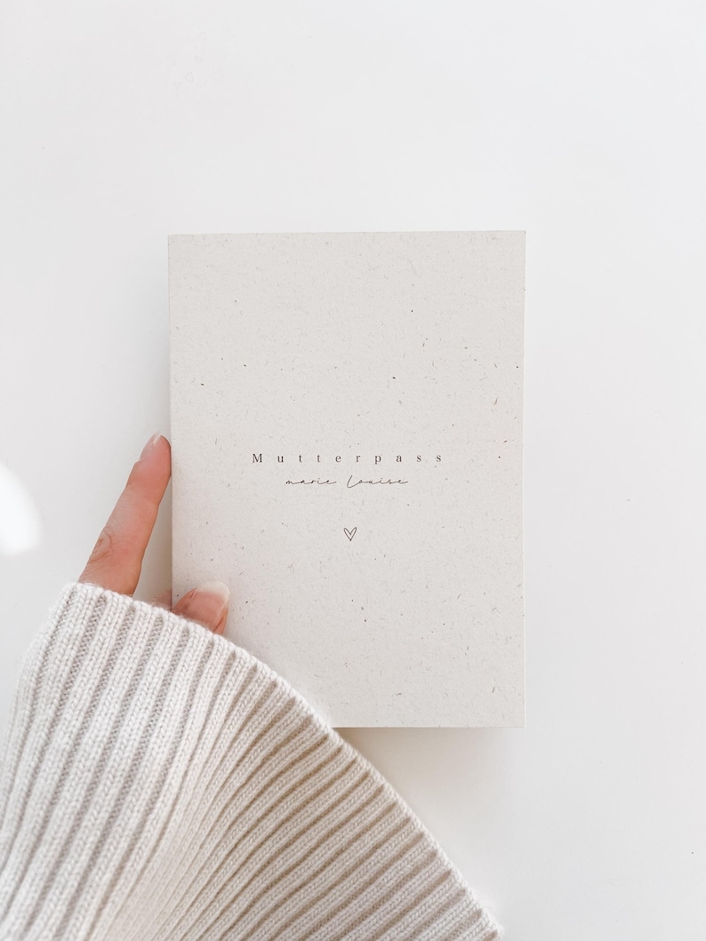 Puede incluir: Una libreta blanca con el texto "Mutterpass" y "marie louise" escrito en ella. Un peque&ntilde;o coraz&oacute;n est&aacute; dibujado debajo del texto.