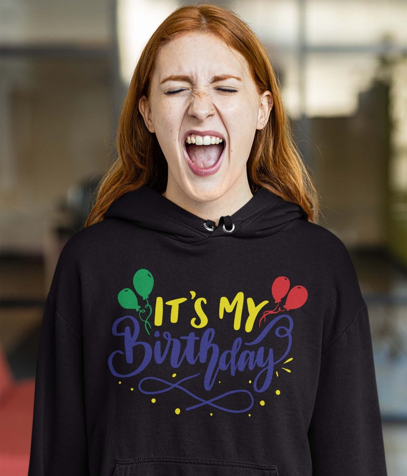 May include: Black hooded sweatshirt with the text "IT'S MY Birthday" in yellow, blue, and green, with balloon graphics. The sweatshirt is worn by a person with red hair.
