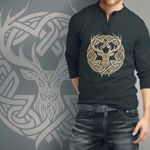 May include: A dark gray long-sleeve shirt with a gold deer head design inside a Celtic knot pattern. The shirt has a button-up collar.