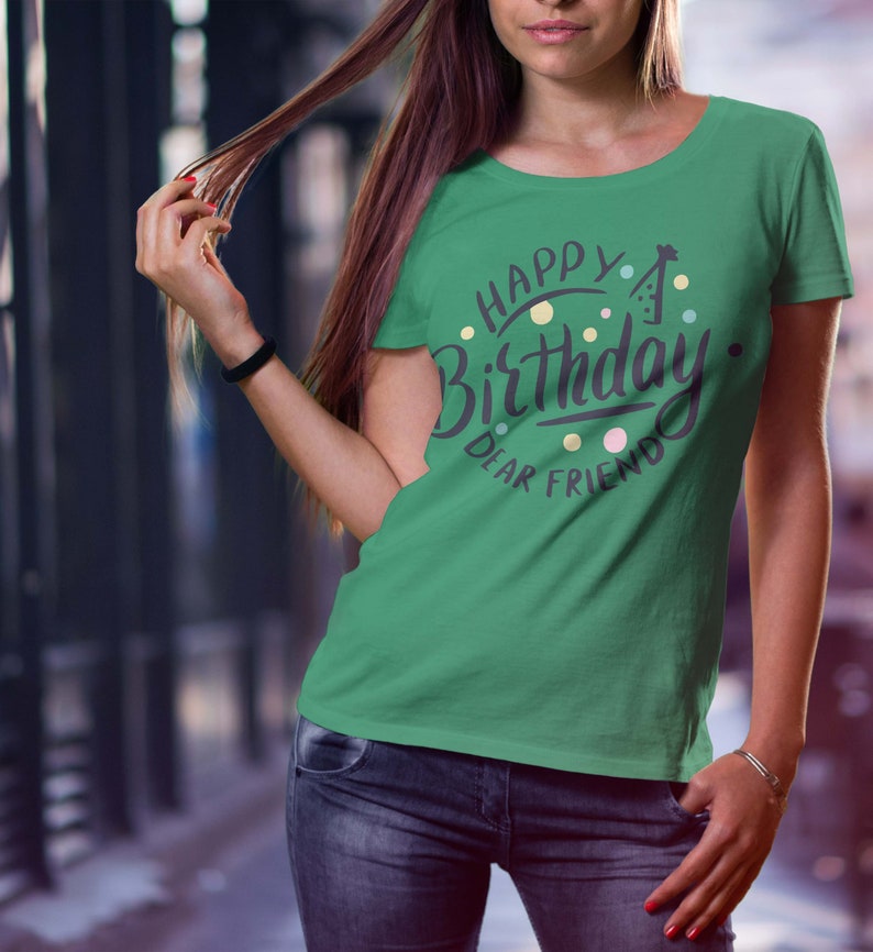 May include: A green t-shirt with the words "Happy Birthday Dear Friend" in a circular design. The text is in a dark purple script with colorful polka dots and a party hat graphic. The shirt is being worn by a person.