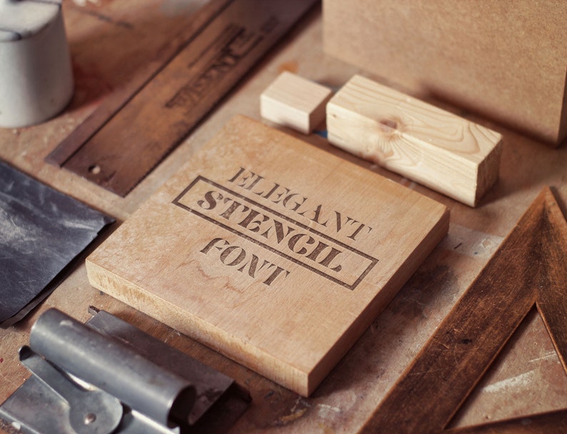 Puede incluir: Un bloque de madera con las palabras "Elegant Stencil Font" grabadas en &eacute;l. El bloque est&aacute; rodeado de otros objetos de madera y herramientas sobre una superficie de madera.