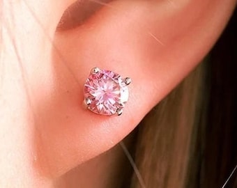 May include: A close-up of a person's ear with a small pink gemstone earring. The earring is a simple stud style with a round, faceted gemstone.