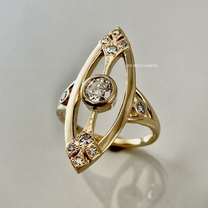 May include: A gold ring with a large, round, clear diamond in the center. The ring is set with smaller diamonds around the center stone and on the band. The ring is in the shape of an eye.
