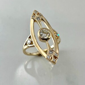 May include: A gold ring with a large oval-shaped diamond in the center. The ring is set with smaller diamonds around the center stone and on the band. The ring is designed in a unique, eye-catching style.