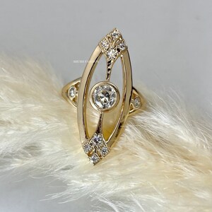 May include: A gold ring with a large, round, clear gemstone set in a delicate, oval-shaped frame. The frame is adorned with smaller, clear gemstones.