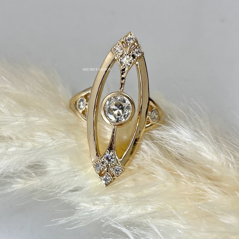 May include: A gold ring with a large, round, clear gemstone set in a delicate, oval-shaped frame. The frame is adorned with smaller, clear gemstones.