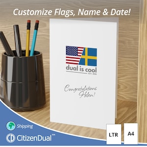 Puede incluir: Una tarjeta de felicitación blanca con las banderas estadounidense y sueca, el texto "dual is cool" y "Congratulations Helen!". La tarjeta está en posición vertical, con un portalápices y bolígrafos en el fondo. La tarjeta también tiene el texto "Customize Flags, Name & Date!"