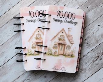 May include: Two spiral-bound savings challenge notebooks. The covers feature watercolour illustrations of houses with the text "10,000 Savings Challenge" and "20,000 Savings Challenge". The notebooks have pink accents and black spiral bindings.