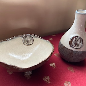 May include: A white ceramic bowl with a brown rim and three feet, and a white ceramic vase with a brown rim and a brown band around the bottom. Both pieces have a stylized tree design.