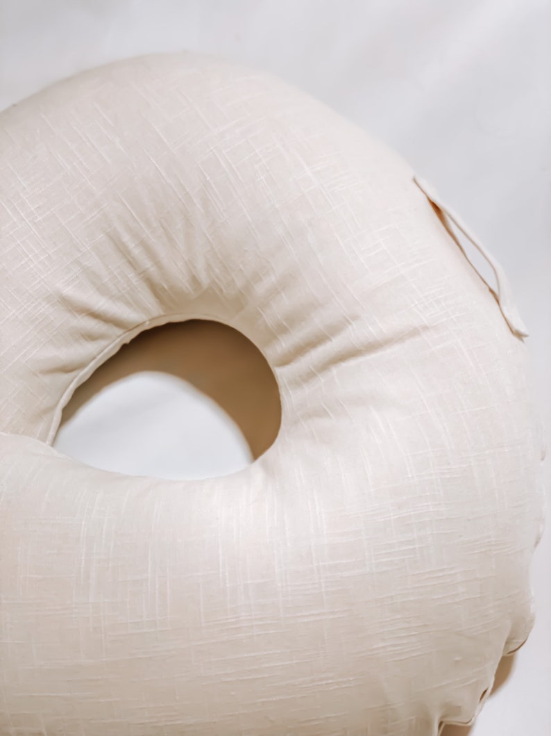 K&ouml;nnte beinhalten: Ein cremefarbenes, donutf&ouml;rmiges Kissen mit einem Bezug aus strukturiertem Stoff.