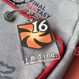 May include: A clear acrylic keychain with a red and black swirl design and the number 16. The text "I'm fine." is printed on the keychain.