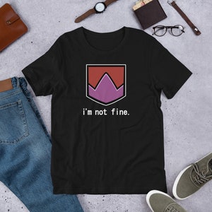 May include: Black t-shirt with a shield-shaped graphic in red, purple, and white, and the text "i'm not fine." The shirt is made of a soft material and is suitable for casual wear.