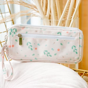 Puede incluir: Una bolsa rosa con cremallera con un patrón floral y una pequeña asa. La bolsa está hecha de un tejido suave y tiene una cremallera blanca.