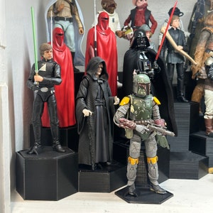 May include: A collection of Star Wars action figures displayed on black hexagonal shelves. The figures include Luke Skywalker, Darth Vader, Boba Fett, and others. The figures are posed in various action poses.