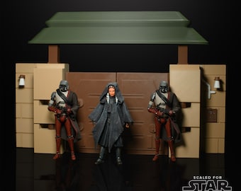 May include: Three action figures stand in front of a brown wooden gate with a green roof. Two figures are wearing black and red armour and holding weapons. The figure in the middle is wearing a black robe and has a hood. The text "SCALED FOR STAR WARS THE BLACK SERIES" is at the bottom of the image.