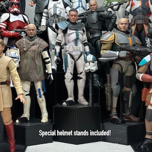 May include: A collection of Star Wars action figures, including a blue and white clone trooper, a brown-clad Jedi, and a black-clad bounty hunter. The figures are displayed on a black hexagonal stand with the text "Special helmet stands included!" printed on the front.