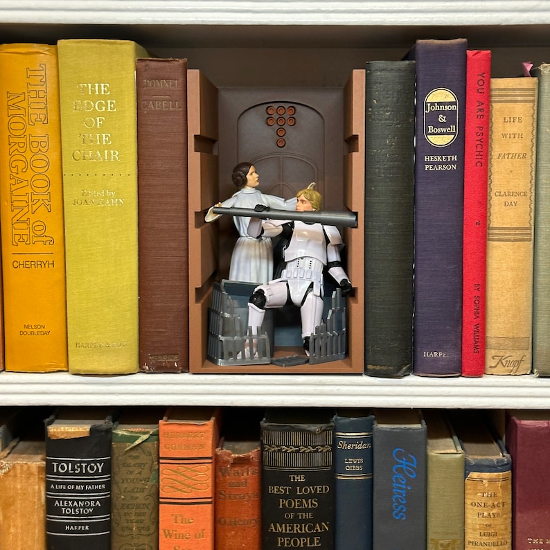 May include: A brown wooden bookend with a Star Wars themed design. The bookend features a scene of a Stormtrooper and a woman in a white dress standing in a doorway. The bookend is on a bookshelf with other books.