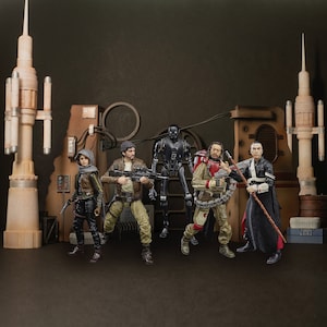 Può includere: Un gruppo di sei action figure, tra cui un robot nero, una donna con una giacca marrone, un uomo con una giacca marrone, un uomo con una giacca rosso e nera, un uomo con una tunica nera e una donna con una giacca marrone. Le figure sono in una varietà di pose d'azione e sono tutte in piedi su una superficie marrone.