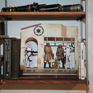 May include: A wooden shelf displays Star Wars collectibles, including lightsabers, action figures, and a diorama. The figures include a clone trooper, Jedi, and Yoda. Books are on the shelf, including "The Diamond Throne" and "One Thing".