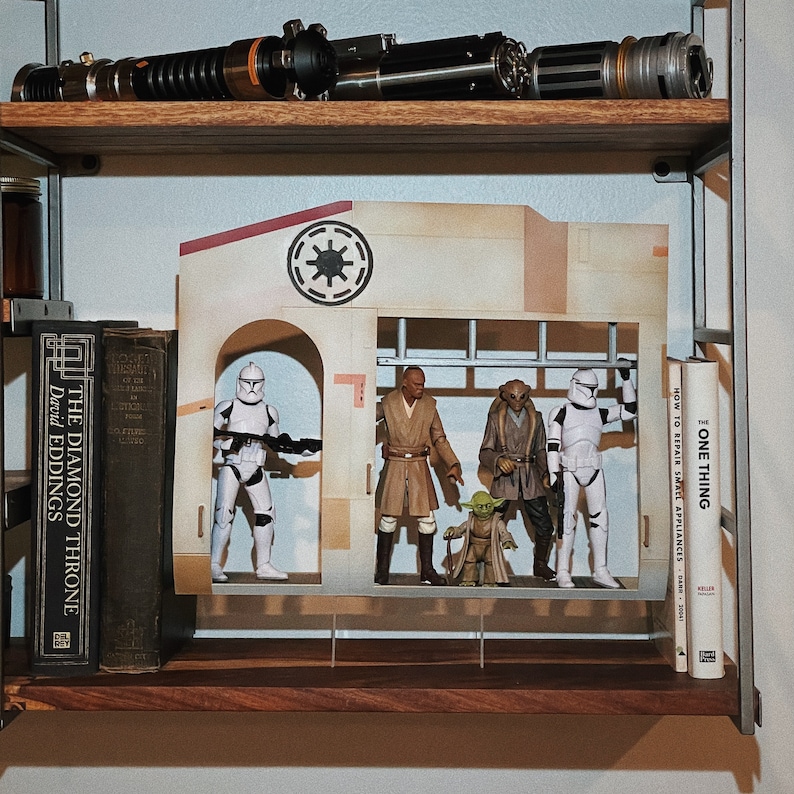 May include: A wooden shelf displays Star Wars collectibles, including lightsabers, action figures, and a diorama. The figures include a clone trooper, Jedi, and Yoda. Books are on the shelf, including "The Diamond Throne" and "One Thing".