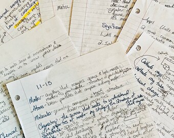 Puede incluir: Un conjunto de notas manuscritas en papel rayado, con varios conceptos y fórmulas científicas. Las notas cubren temas como la energía, la materia y la química, con diagramas y anotaciones. Los papeles están dispersos.