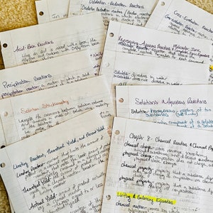 May include: A collection of handwritten notes on lined paper, detailing chemistry concepts such as acid-base reactions, precipitation, and solution stoichiometry. The notes are in black ink with highlighted sections, and the pages are scattered on a textured surface.