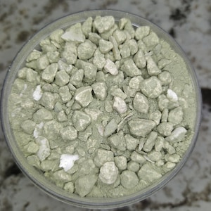 May include: A close-up of a glass jar filled with small, light green and white stones. The stones are irregularly shaped and have a rough texture.