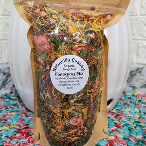 May include: A clear stand-up pouch filled with a colorful organic forage mix containing dried calendula, roses, spinach, nettle leaf, strawberries, carrots, and beets. The label reads Naturally Crabby Organic Forage Food Foraging Mix.