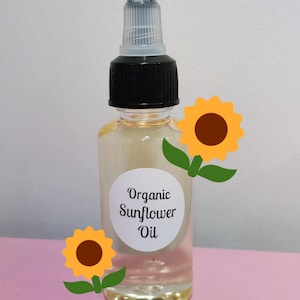 May include: A clear glass bottle of organic sunflower oil with a black cap and a white label. The label reads "Organic Sunflower Oil". Two cartoon sunflowers are placed on the image. The bottle is on a pink surface.