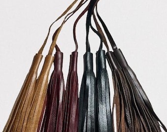 May include: Six leather tassels in various colors, including brown, burgundy, black, and tan. The tassels are made of thin strips of leather that are tied together at the top.