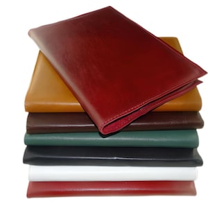 May include: A stack of eight leather-bound folders in various colors, including red, brown, tan, green, black, and white.