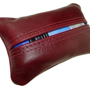 Könnte beinhalten: Ein dunkelroter Leder-Tischtuchhalter mit einem blauen Taschentuch-Einsatz. Der Halter hat ein genähtes Design und eine Klappe, die sich öffnet, um den Taschentuchhalter zu enthüllen.