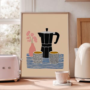 Op de afbeelding: Een roze broodrooster in retrostijl met chromen accenten staat naast een ingelijste print van een koffiepot en mokken. Een crèmekleurige elektrische waterkoker en een kleine kop staan ook op het houten aanrecht. De print toont een zwarte koffiepot en twee mokken.