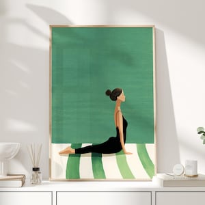 Op de afbeelding: Een ingelijste kunstdruk toont een persoon in een yogahouding op een gestreepte mat. De persoon draagt een zwarte outfit tegen een groene achtergrond. Het kunstwerk zit in een houten lijst, geschikt voor interieurdecoratie.