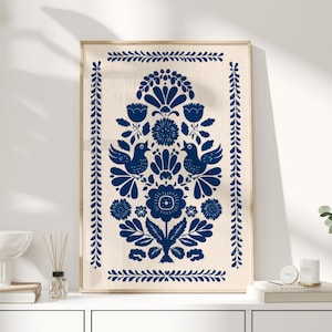 Puede incluir: Una impresión artística enmarcada con un diseño floral simétrico en azul marino sobre un fondo crema. El diseño incluye pájaros estilizados, flores y follaje, enmarcado por un borde azul marino. La obra de arte se exhibe sobre una superficie blanca.