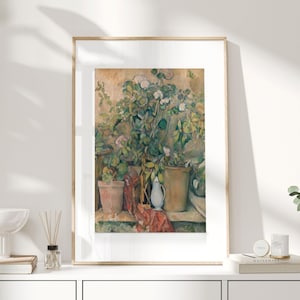 Op de afbeelding: Een ingelijste aquarel schildering toont een stilleven van potplanten en bloemen. Het kunstwerk toont terracotta potten, een witte kan en een rode doek. De schildering heeft een warm kleurenpalet met groen, bruin en wit.