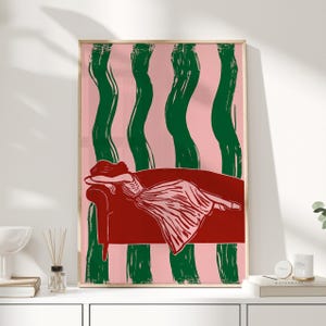 Peut inclure: Impression d'art représentant une femme allongée sur un canapé rouge. Le fond est rose avec des coups de pinceau verticaux verts. La femme porte une robe, et l'impression est encadrée dans un cadre en bois clair.
