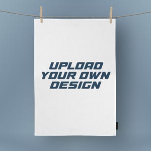 May include: A white rectangular fabric with the text "UPLOAD YOUR OWN DESIGN" in blue, hanging from a clothesline with wooden clothespins. The background is a solid light blue.