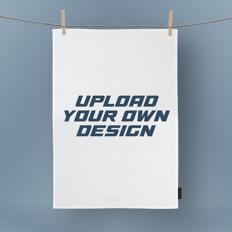 May include: A white rectangular fabric with the text "UPLOAD YOUR OWN DESIGN" in blue, hanging from a clothesline with wooden clothespins. The background is a solid light blue.